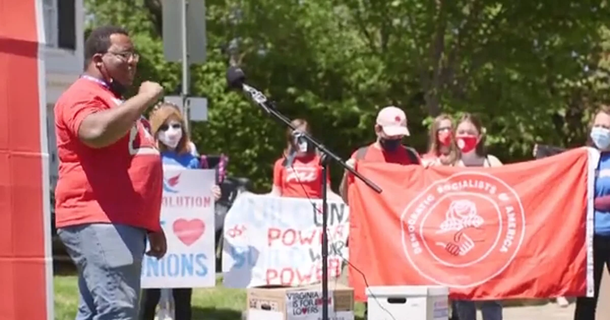 A speaker in a red shirt addresses a crowd at a Metro DC DSA rally, with a 